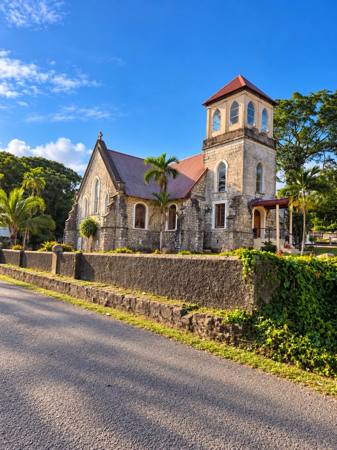 A stone church with a square bell tower and warm-coloured roof stands beside the road.