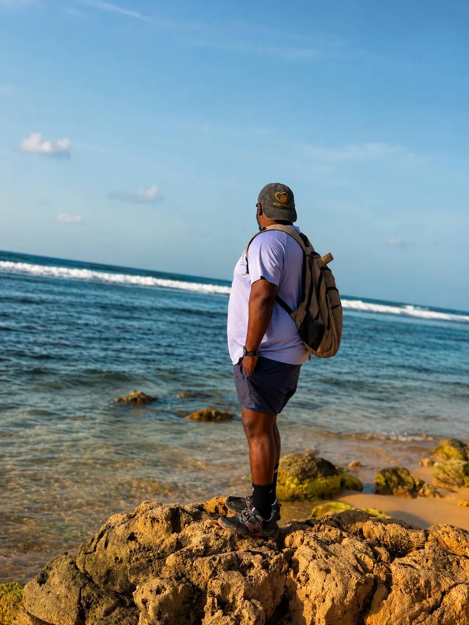A Lifestyle Hiker taking in the Hellshire coastline, rocky shore, calm water, and wide open sky