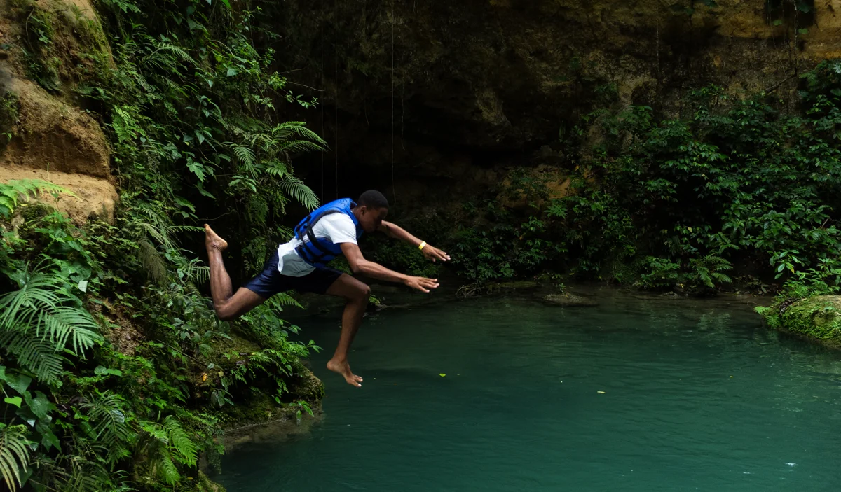 A swimmer jumping into a forest pool at Island Gully Falls / Blue Hole in Jamaica